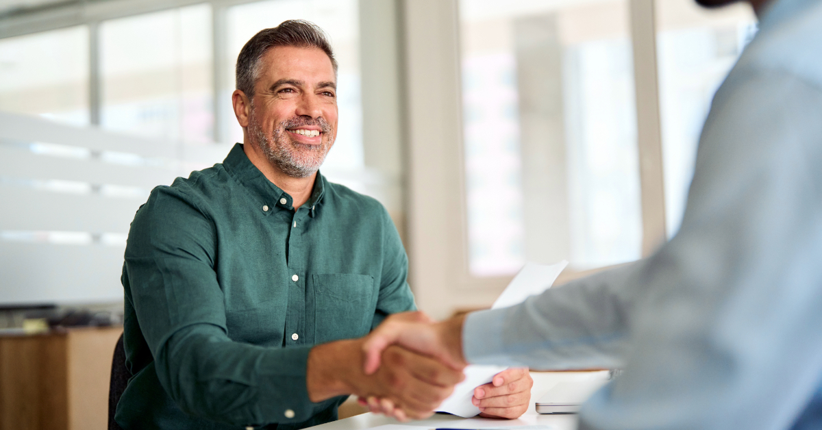A man smiles while shaking hands with another person across a desk in an office setting, illustrating the benefits of legal funding.