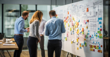 Four people collaborate at a whiteboard covered in notes and diagrams in a modern office setting, strategizing for success in e-commerce with an emphasis on exceptional branding.