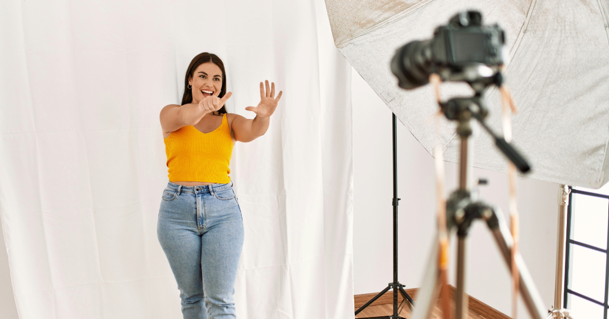 A woman in a yellow top and jeans poses in front of a camera on a tripod with studio lighting in the background, offering tips for making money fast with stock photography.