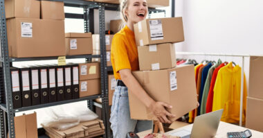 In a bustling storage room, a person carrying several packages beams with satisfaction, embodying the spirit of ecommerce ventures.