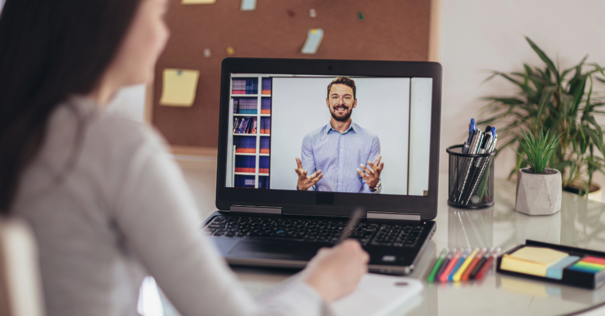 A person participates in an online video call with a man on a laptop screen, discussing tips for making money fast with online courses. A corkboard and plant are in the background.