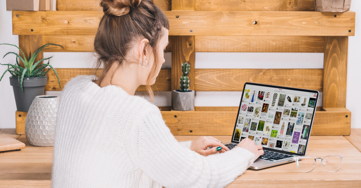 A woman in a white sweater sits at a wooden desk, using a laptop displaying a grid of plant images alongside tips for making money fast on Pinterest.