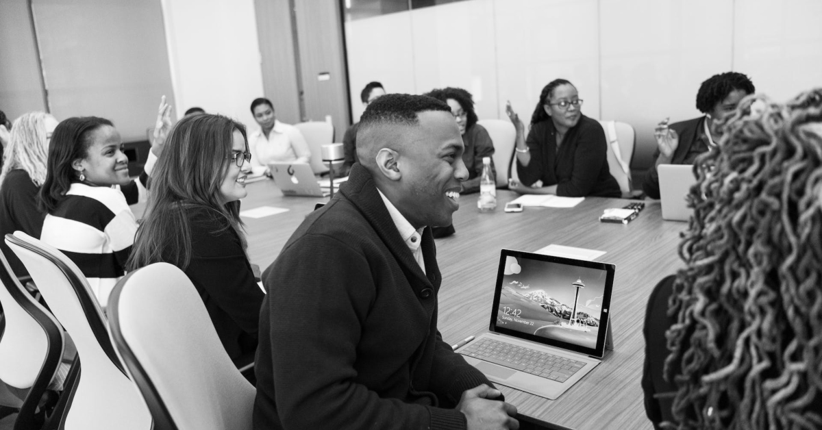 A group of people sitting around a large conference table, engaged in discussion about smart business strategies, with laptops and notebooks in front of them.