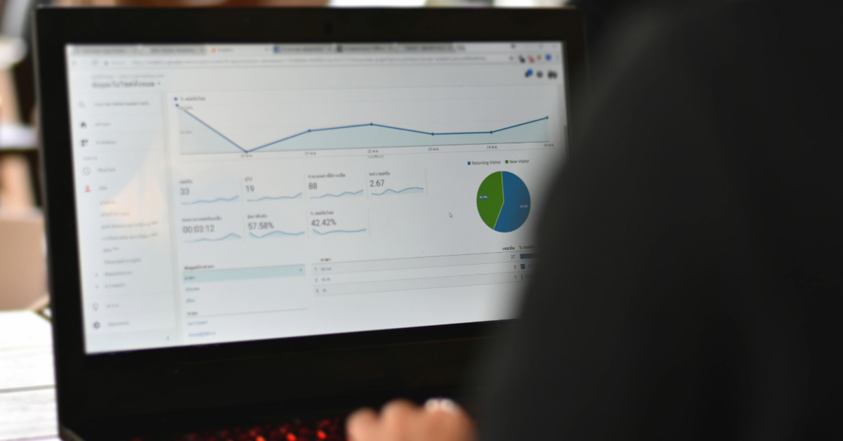 A small business owner sits in front of a laptop displaying analytical charts and graphs on the screen, monitoring SEO performance through GA4.