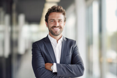 A man in a suit stands confidently, smiling with arms crossed in a brightly lit corridor, embodying the success of DTC business strategies.