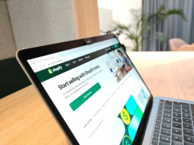 A laptop showcasing the Shopify homepage sits on a wooden table, surrounded by innovative ideas and tools to automate your ecommerce website, setting the stage for success in 2024.