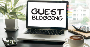 A laptop on a desk showcases the words "Guest Blogging," perfectly blending with an ecommerce vibe. Nearby, a potted plant, smartphone, calculator, and a steaming cup of coffee create an ideal Shopify workspace.