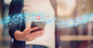 A person holds a smartphone with illustrated social media icons and connections floating above, symbolizing seamless online interactions that drive ecommerce success on Shopify.