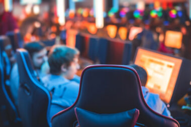 In a dimly lit room, enthusiasts sit in gaming chairs, their eyes glued to monitors. Beyond the digital thrills, whispers of Shopify and ecommerce strategies fill the air, as ideas for DTC campaigns flow seamlessly with the gaming action.