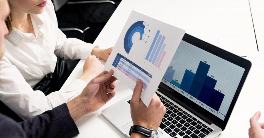 Two people review printed charts while a laptop displays a bar graph, illustrating the growth trends in their DTC ecommerce venture on Shopify.