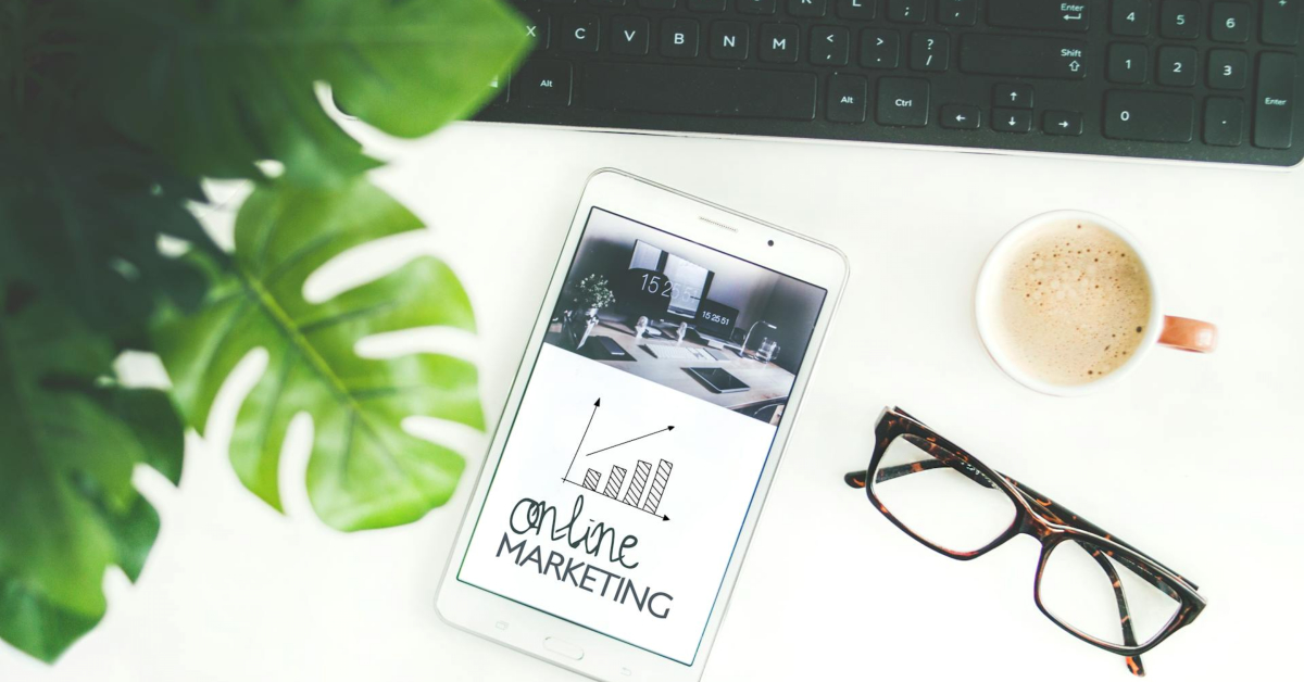 A tablet showcasing "online marketing" alongside a graph sits on a desk with essentials like a keyboard, coffee cup, plant, and glasses—an ideal setup to improve your SEO strategy.