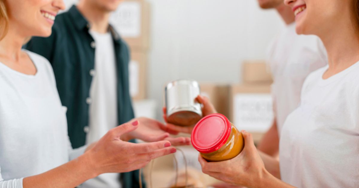 Four people swapping canned goods and jars in a room decked with cardboard boxes in the background, each item meticulously organized like custom branded merchandise, reflecting their commitment to community spirit.