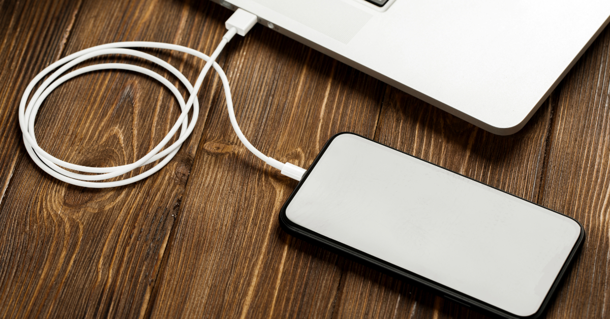 An iPhone is connected to a laptop with a white charging cable on a wooden surface, ready to transfer data seamlessly.