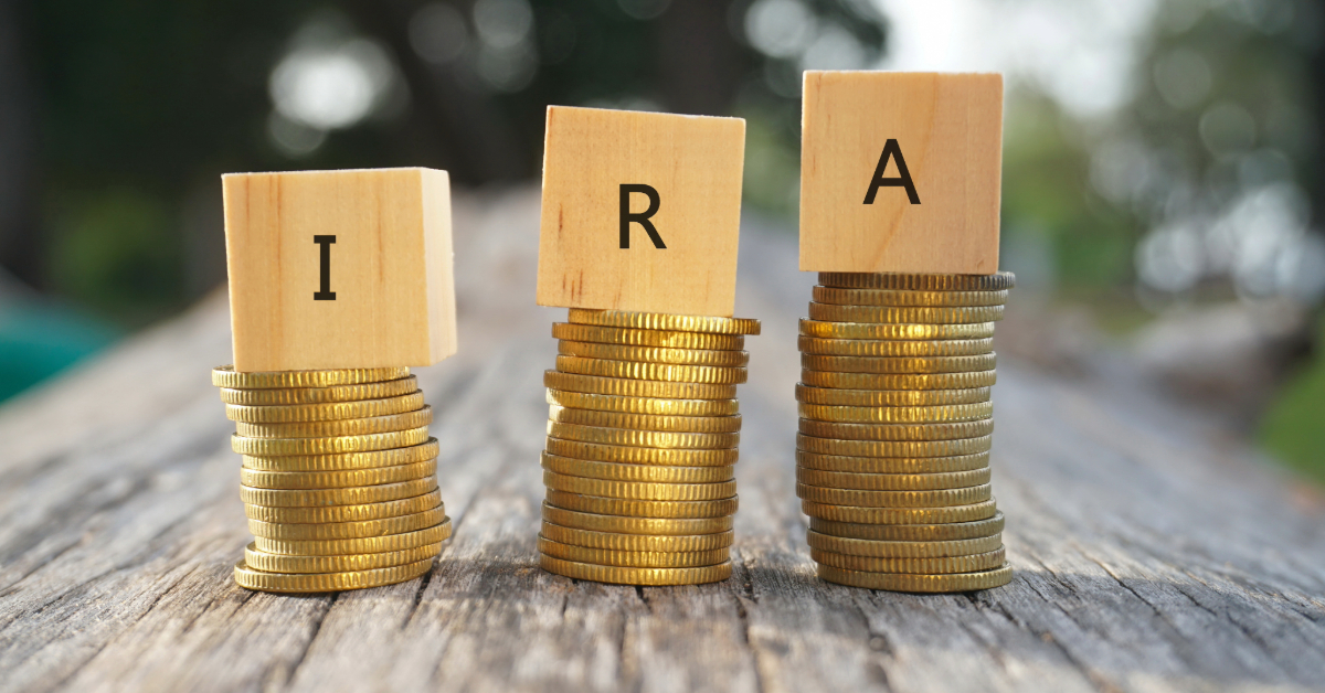 Stacks of gold coins, a gleaming nod to precious metals, with wooden blocks displaying the letters I, R, and A on a rustic surface against a blurred background.
