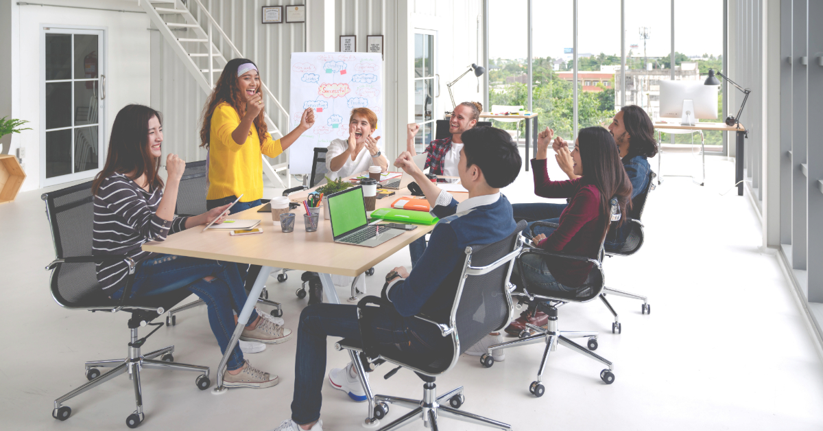 A group of people sit around a conference table in a modern office, engaging in a lively discussion that fuels productivity. Laptops and paperwork are visible on the table, illustrating an efficient workplace buzzing with ideas.