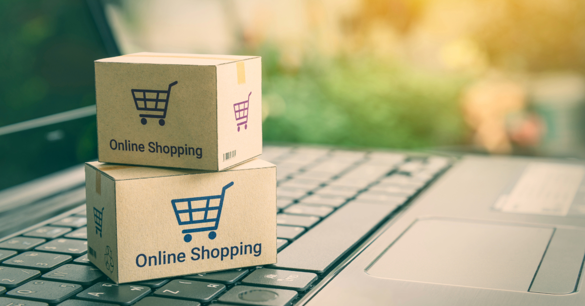 Two cardboard boxes with shopping cart icons and "Online Shopping" text rest on a laptop keyboard, symbolizing key strategies in the e-commerce business.