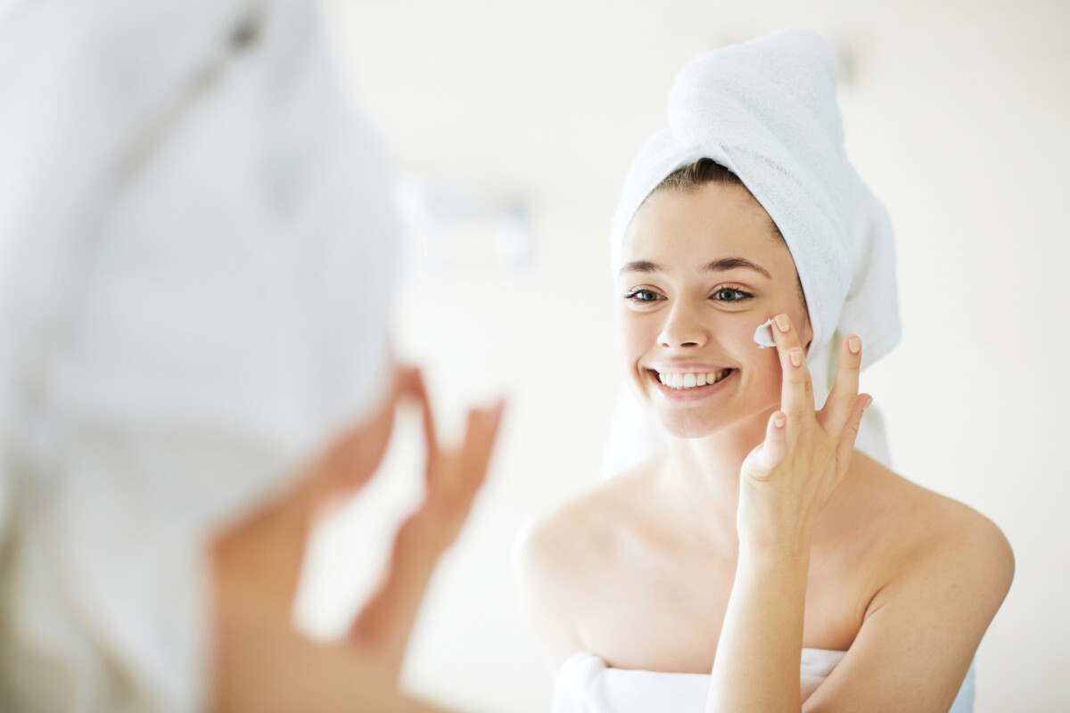 A woman with a towel on her head applies cream to her face while looking in a mirror, reflecting the personalized trends shaping Australia's online beauty market.