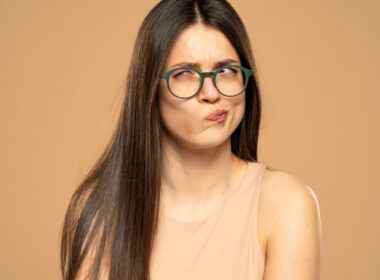 A person with long hair and glasses displays a puzzled expression against a beige background, perhaps contemplating the latest funwithfeet reviews.