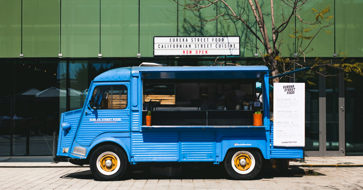 A blue food truck labeled "Eureka Street Food" is parked in front of a green building. The sign above reads "California Street Cuisine Now Open." This vibrant vehicle is more than just one of many food trucks; it's a destination designed to drive sales with its mouthwatering offerings.