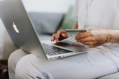 A person sits on a couch, using a laptop and holding a credit card, exploring the latest Ecommerce trends.