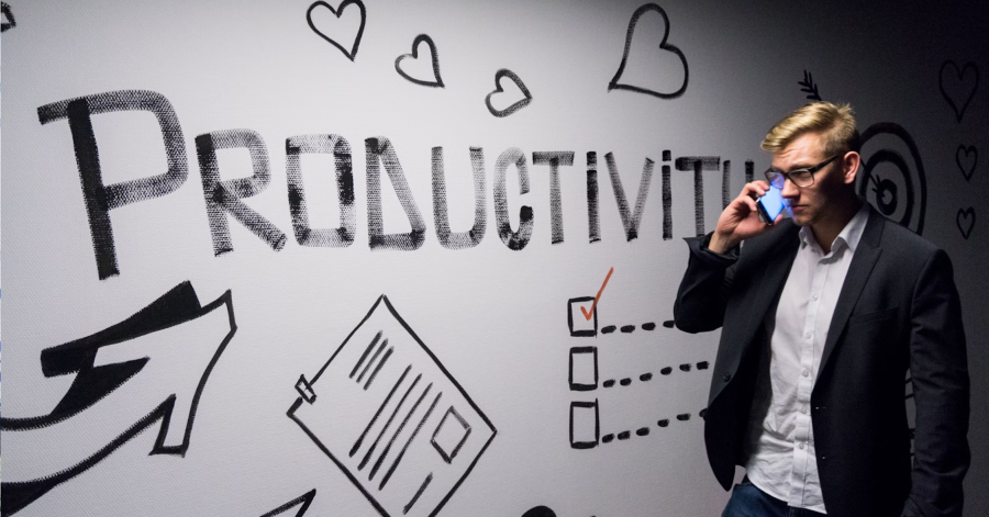 Man in glasses talking on phone, standing near a wall with "PRODUCTIVITY" and various doodles, including arrows, checklists, and strategies for enhancing monitoring systems.