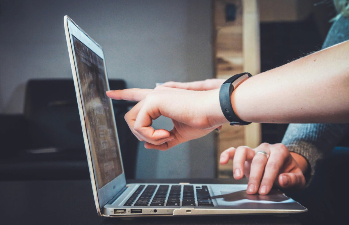 Two people interact with a laptop; one hand points at the screen while another types on the keyboard, showcasing helpful tools for business leaders to enhance productivity.