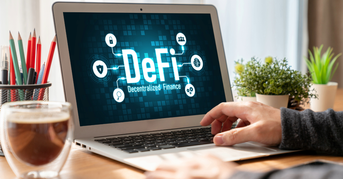 A person using a laptop displaying the words "DeFi Decentralized Finance" on the screen, with LINK charts open, a coffee cup, potted plant, and office supplies nearby.