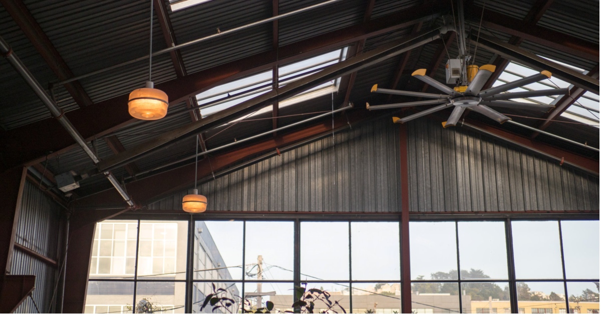 Industrial-style ceiling with exposed beams, two round light fixtures, a large ceiling fan, and floor-to-ceiling windows—ideal for optimizing warehouse efficiency with abundant natural light.