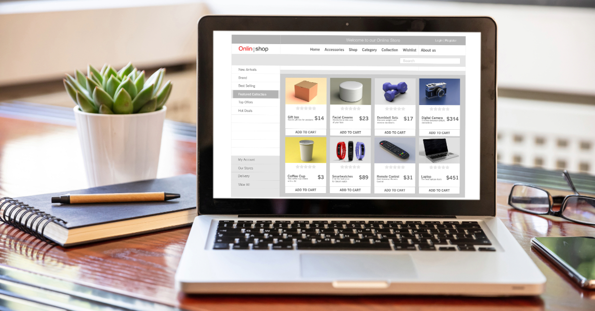 A laptop on a desk displays an online shopping website, showcasing various products and prices; perfect inspiration for launching a Shopify store. A plant, notebook, and pen are placed beside the laptop.