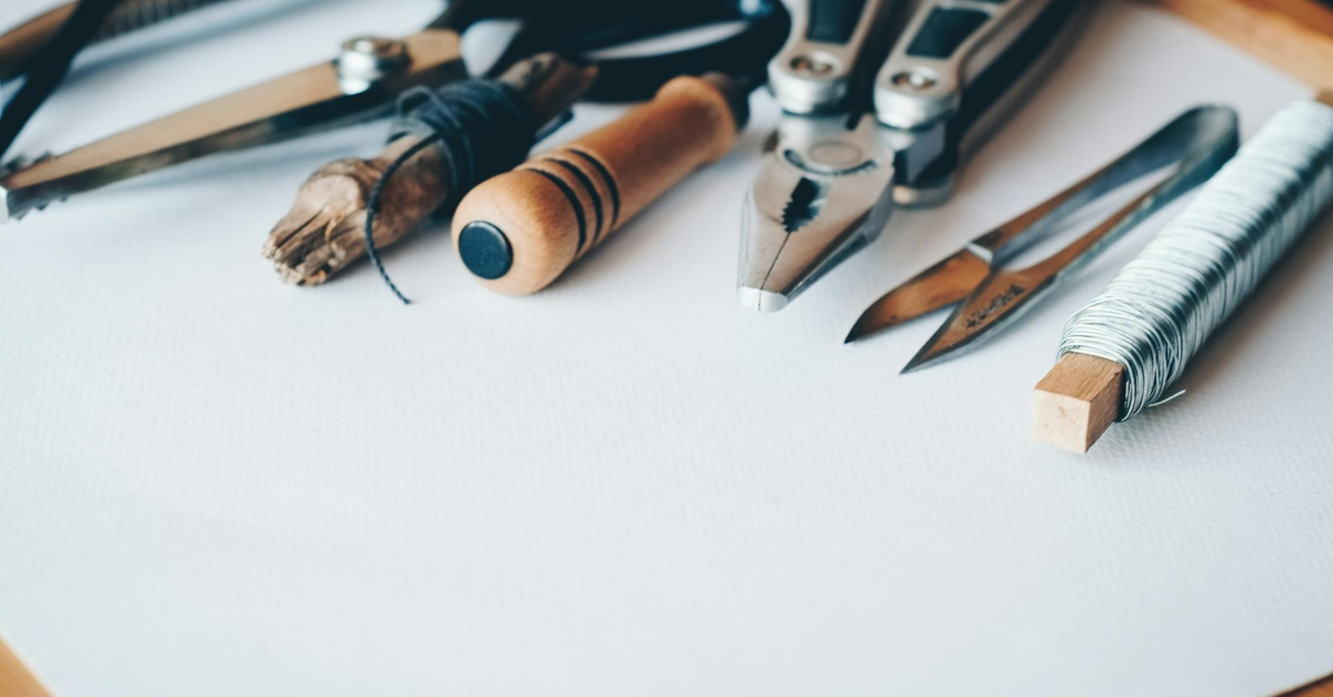 A variety of hand tools, string, pliers, scissors, and wire—perfect for those looking to buy business equipment—are arranged in a row on a white surface.