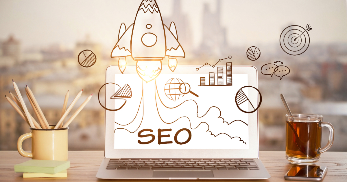 A laptop displaying "SEO" with doodles of graphs, a rocket, and icons sits on a desk with pencils, a notebook, and tea—perfect for tackling 2024 digital marketing mistakes.