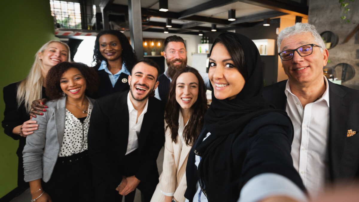 A group of eight professionally dressed people pose for a selfie together in a modern Cynergy BPO office, all smiling at the camera, embodying the spirit of e-commerce outsourcing in the Dominican Republic.