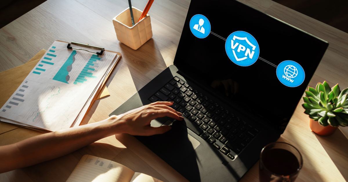 A person uses a laptop displaying VPN icons on a desk with charts, a plant, pencils, and a glass of water, highlighting how to access the web unrestricted or bypass IP bans for secure browsing.