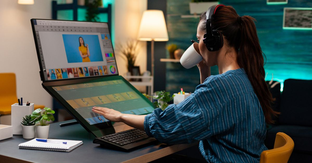 A woman wearing headphones works on a large touchscreen computer, editing photos with an image masking service, while drinking from a mug in a modern, well-lit home office—highlighting its importance for ecommerce businesses.