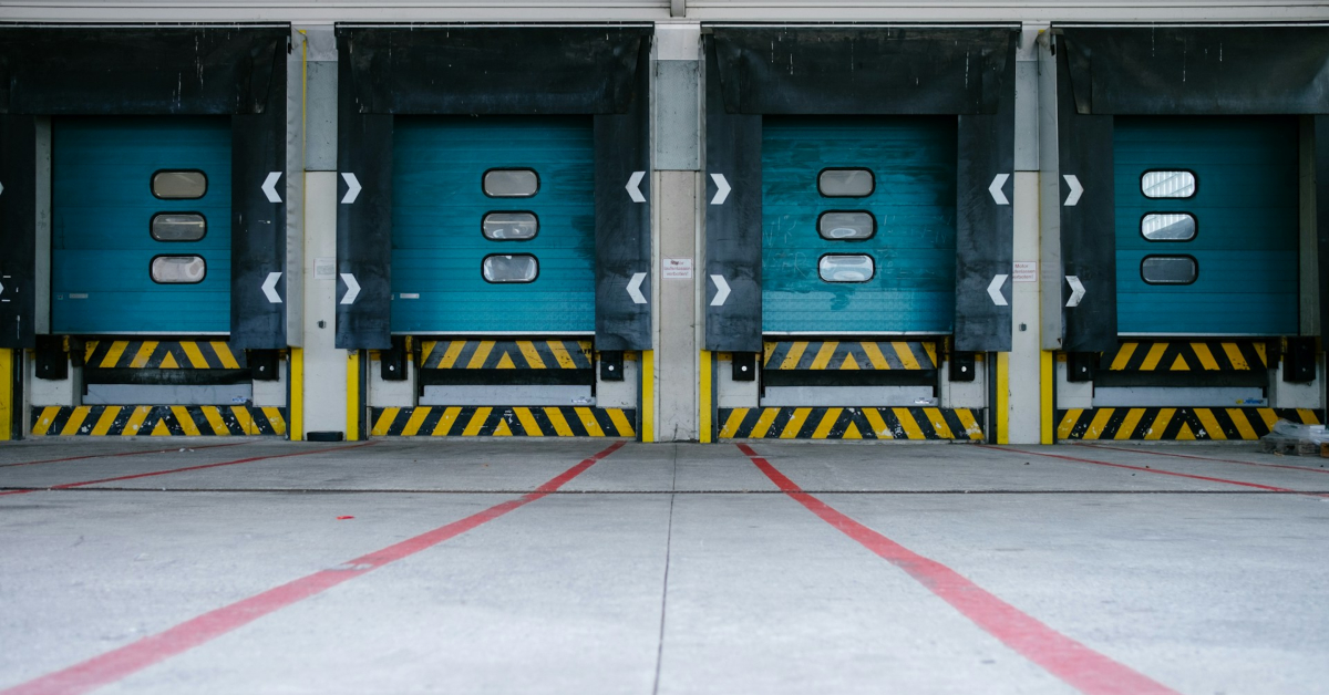A loading dock featuring four closed blue doors, with striped yellow and black bumpers and red guide lines on the ground, serves as the perfect logistics hub designed for efficiency.
