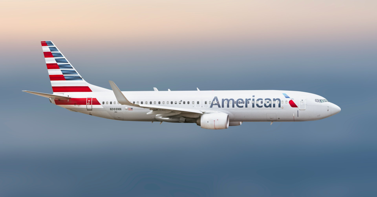 An American Airlines passenger jet flies in a clear sky, proudly displaying the company's logo and red, white, and blue tail—reminding travelers to earn airline rewards and turn clicks to miles with every flight.