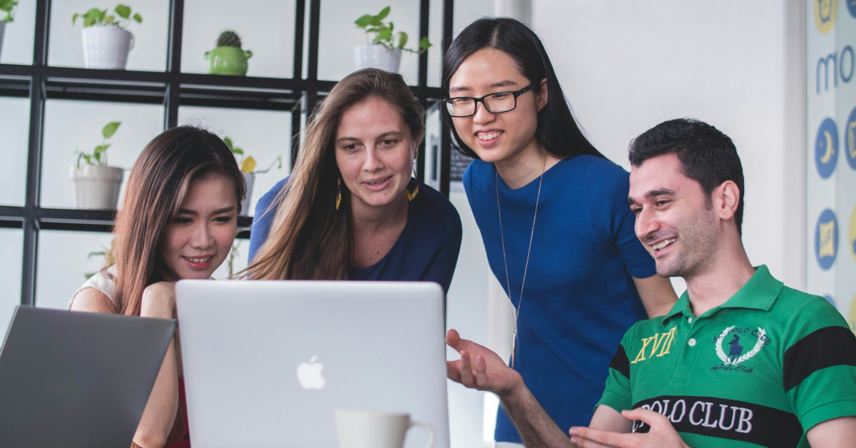 Four people are gathered around a laptop in an office setting, having a discussion about their upcoming product launch and exploring effective online marketing strategies.