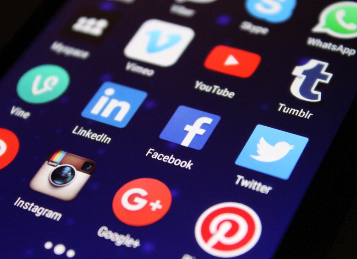A smartphone screen displays various social media app icons, including Facebook, Twitter, Instagram, LinkedIn, Pinterest, and YouTube—essential platforms in 2024 to maximize reach and engagement.