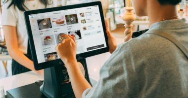 A person expertly navigates a modern POS system at the counter, swiftly selecting food items for purchase, enhancing business efficiency.