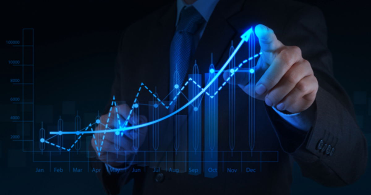 A person in a suit points at a glowing, upward-trending graph on a transparent digital screen, illustrating B2B sales growth and progress over a calendar year.