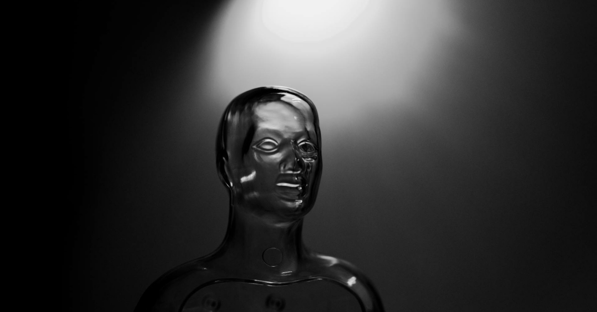 A glossy, black mannequin bust is illuminated by a bright overhead spotlight against a dark background, evoking the futuristic presence of AI Workers in modern Customer Support.