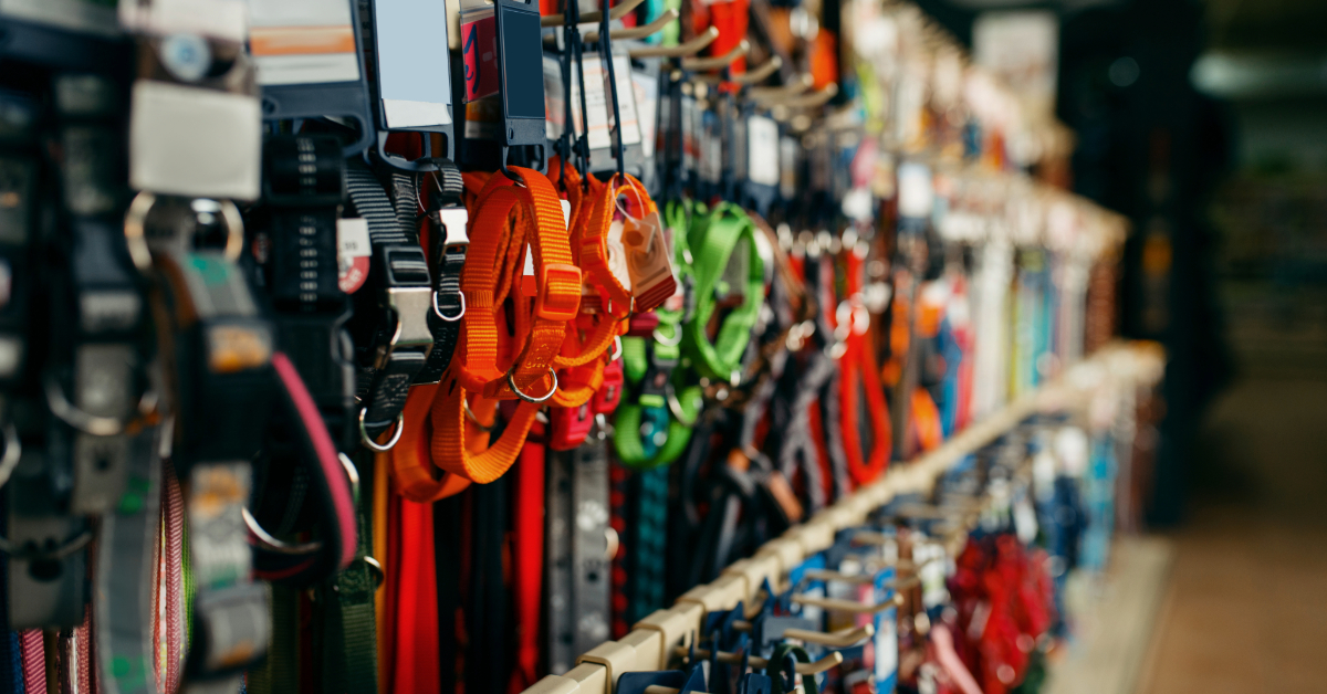 Rows of colorful dog collars and leashes hang on display hooks in a pet supplies store aisle, showcasing the variety available in today's vibrant pet supplies market.
