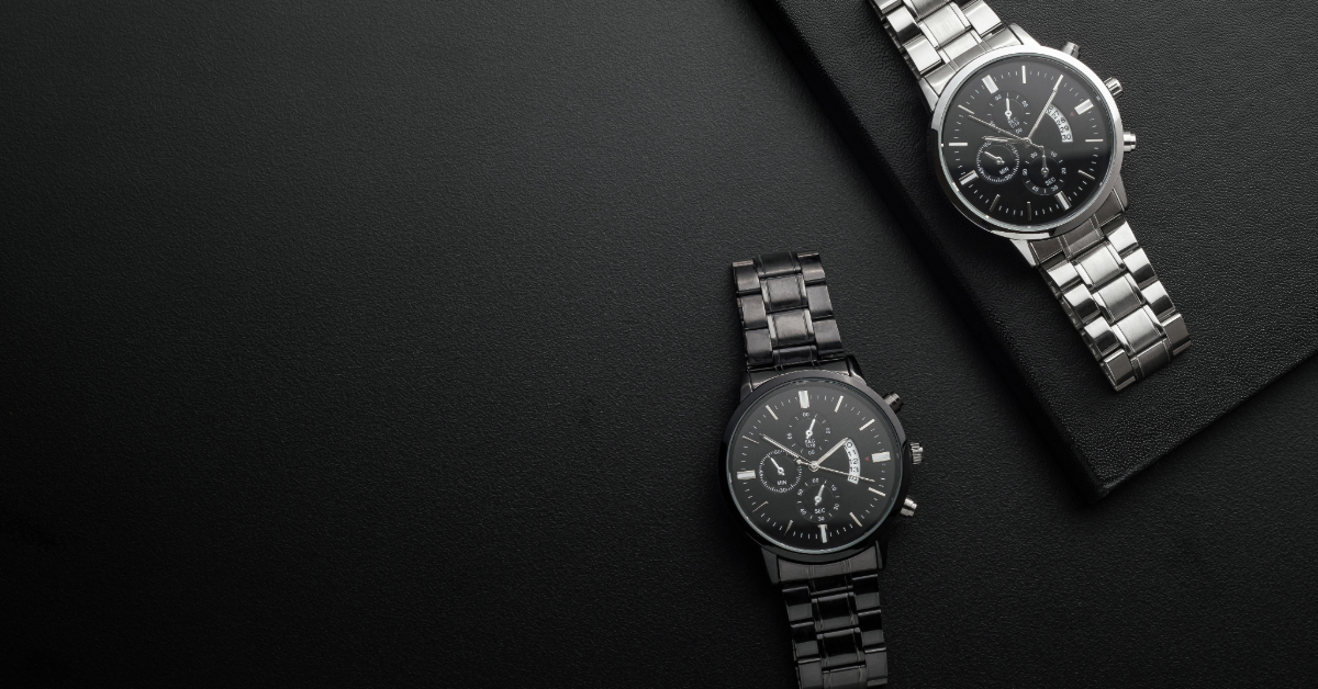 Two black analog wristwatches with metal bands are displayed on a black surface, one on a rectangular object and the other directly on the surface—ideal watch photos that avoid common mistakes when uploading watch photos online.