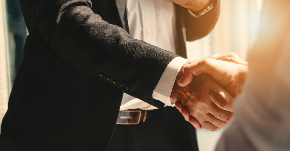 Two people in business attire shaking hands indoors, with sunlight streaming in the background—an ideal moment for sealing a partnership in digital marketing or game development.