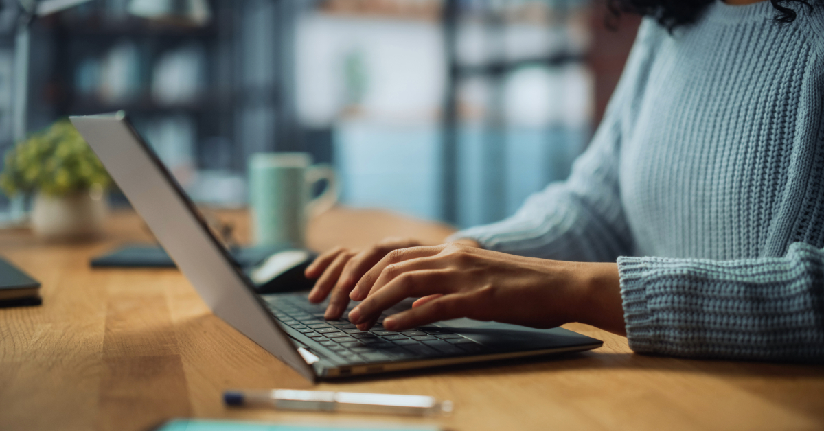 A person wearing a blue sweater types on a laptop at a wooden desk with a pen and mug nearby in a softly lit room, reflecting on optimizing strategies as part of their cost-effective tech leadership approach.