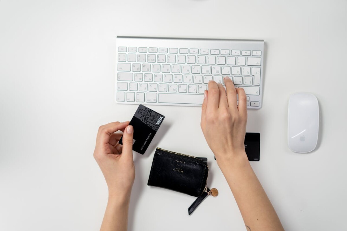 Person holding a credit card and typing on a white keyboard at a tidy desk—perfect setup for running an online business or managing an ecommerce store from home.