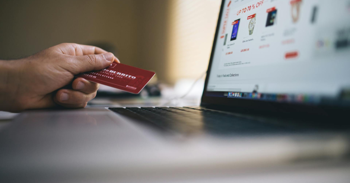 A person holds a credit card in front of a laptop while shopping on an e-commerce website, possibly researching a business to business marketing strategy.