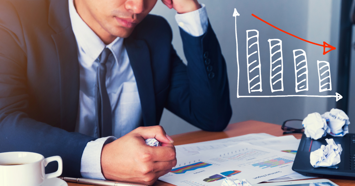 A person in a suit sits at a desk with charts and crumpled papers, next to a downward-trending bar graph illustration, highlighting business mistakes that can impact e-commerce performance.