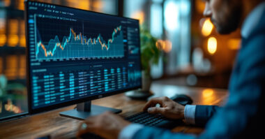 A person in a suit analyzes financial charts and data using a Forex CRM trading solution on a computer monitor at their desk in a modern company office setting.