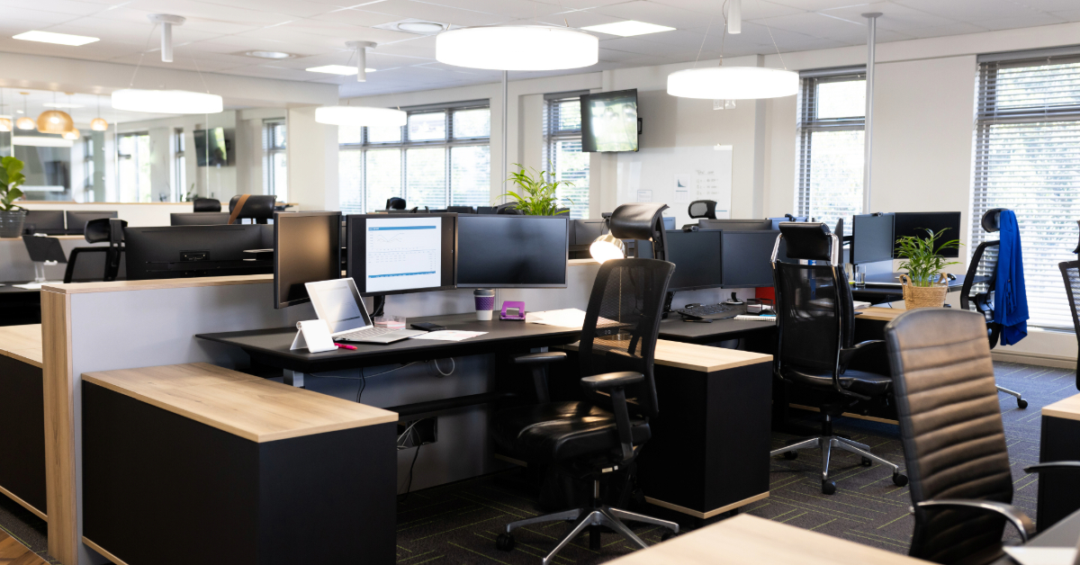 Modern open-plan business space in the UK featuring multiple workstations, computer monitors, office chairs, potted plants, and large windows flooding the modular building with natural light.